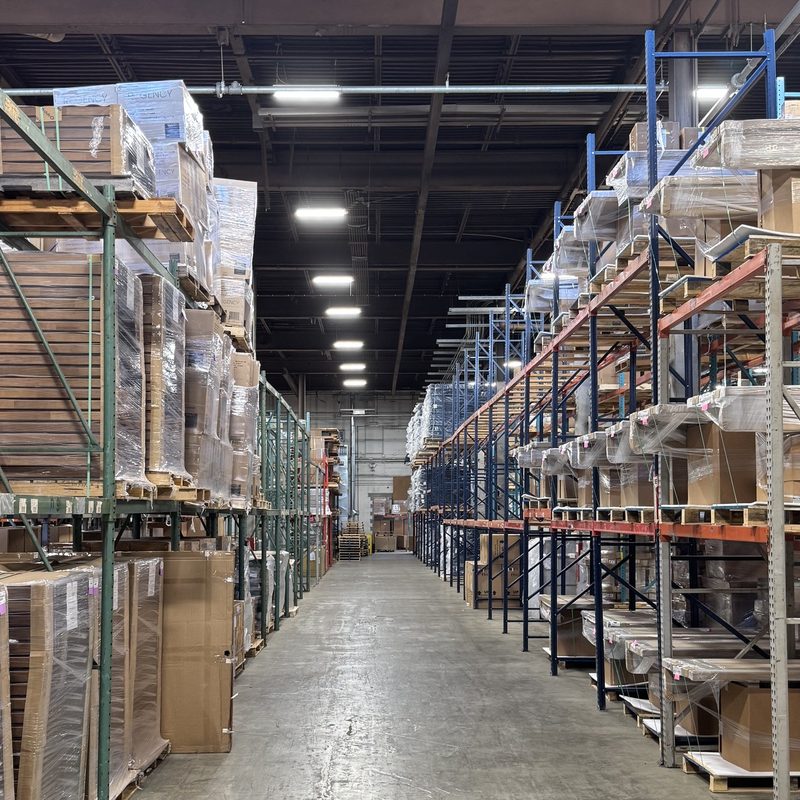Warehouse aisle at the FIG BWI logistics hub, showing shelving stocked with palletized and wrapped furniture inventory